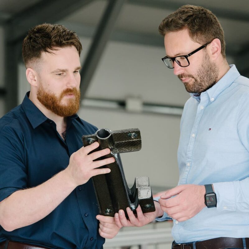 Member of Piran team showing director Mawgan a composite part